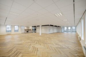 Spacious modern office space on Hiridostraat with herringbone wooden flooring, large windows, and an open kitchenette.